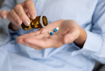 Person holds medication bottle with two blue pills in hand