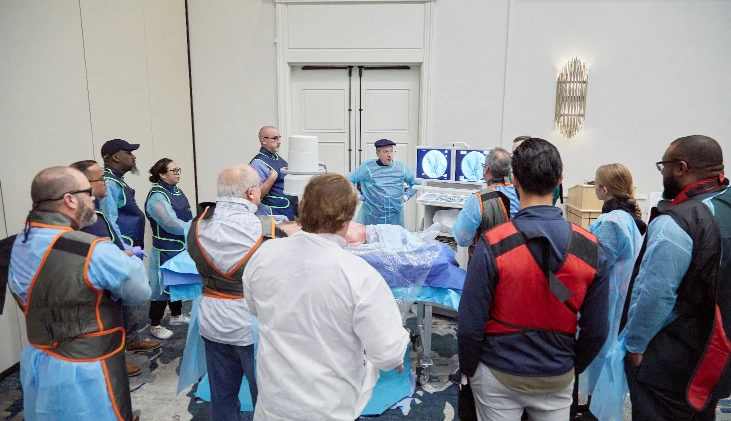Pain Management students stand around cadaver specimen with C-arm machine